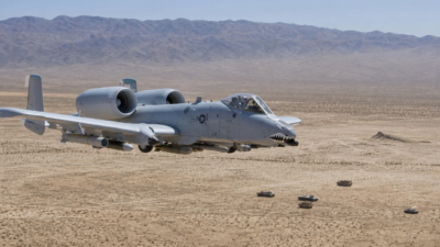 A-10 Thunderbolt II voando baixo sobre área de treinamento desértica sem combate ativo.