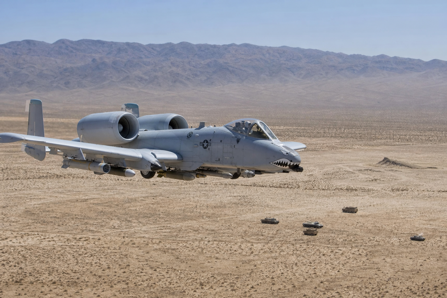A-10 Thunderbolt II voando baixo sobre área de treinamento desértica sem combate ativo.