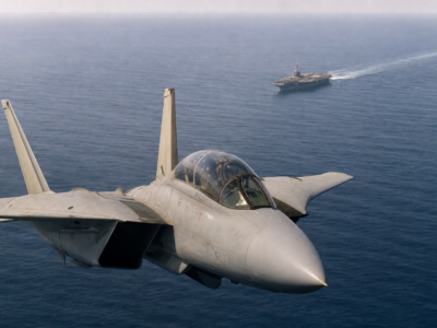 F-14 Tomcat em voo sobre o mar com porta-aviões ao fundo