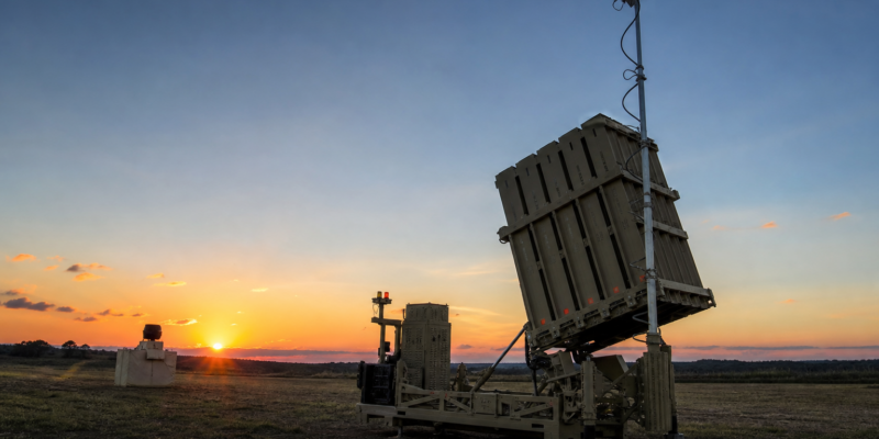 Bateria moderna de defesa aérea em terreno aberto ao entardecer, representando o sistema Iron Dome de forma educativa