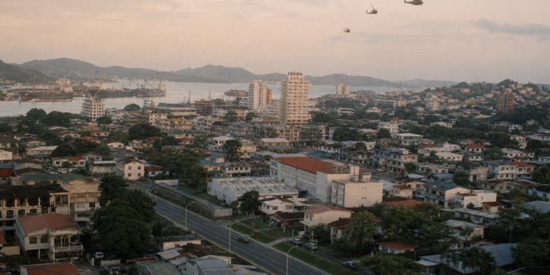 Vista urbana do Panamá no fim dos anos 1980 com helicópteros militares ao longe durante a Operação Just Cause